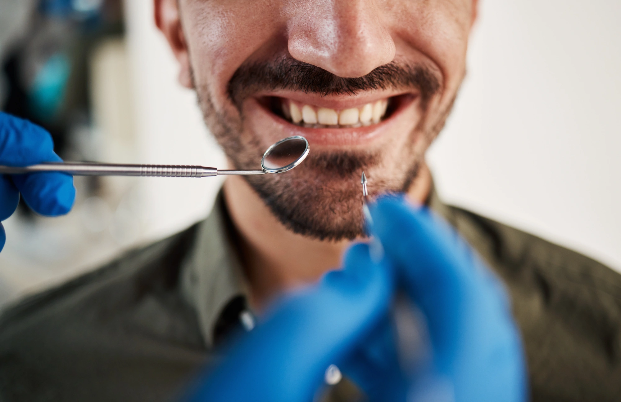 A close-up of a smiling man's face during a dental check-up, with a dentist's hand holding tools gloved in blue