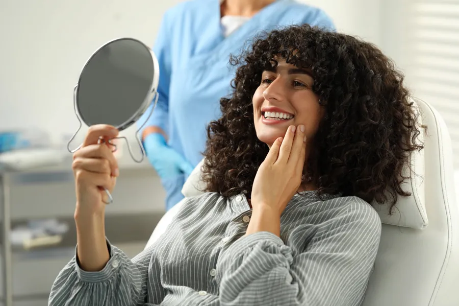 patient smiling with mirror after seeing a cosmetic dentist harrisburg nc 